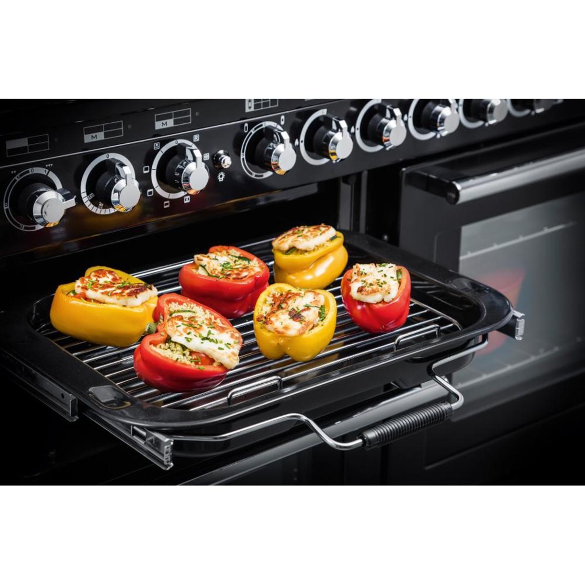 Black and chrome 117380 ENCORE Deluxe 110cm induction range cooker with control knobs, featuring a tray of colorful stuffed bell peppers on a wire rack.