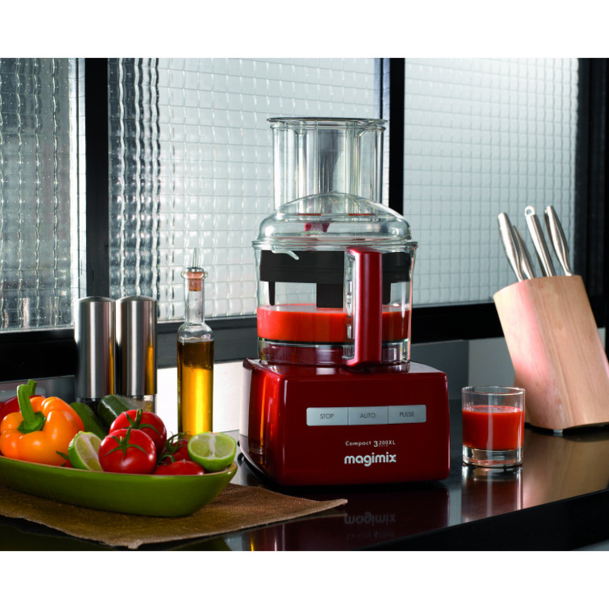 Red Magimix 3200XL food processor with a clear bowl, control panel featuring stop, auto, and pulse settings, surrounded by fresh vegetables and cooking utensils on a kitchen counter.