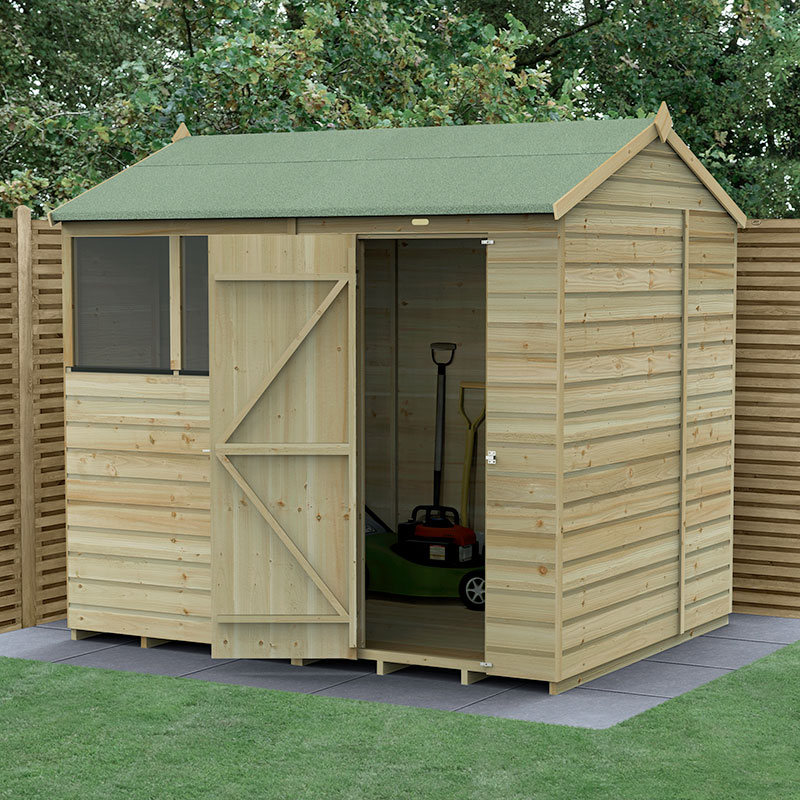 A wooden shed with a reverse apex roof, featuring shiplap cladding, a green felt roof, a side window, and a double door, set on a paved area with grass and surrounding fencing.
