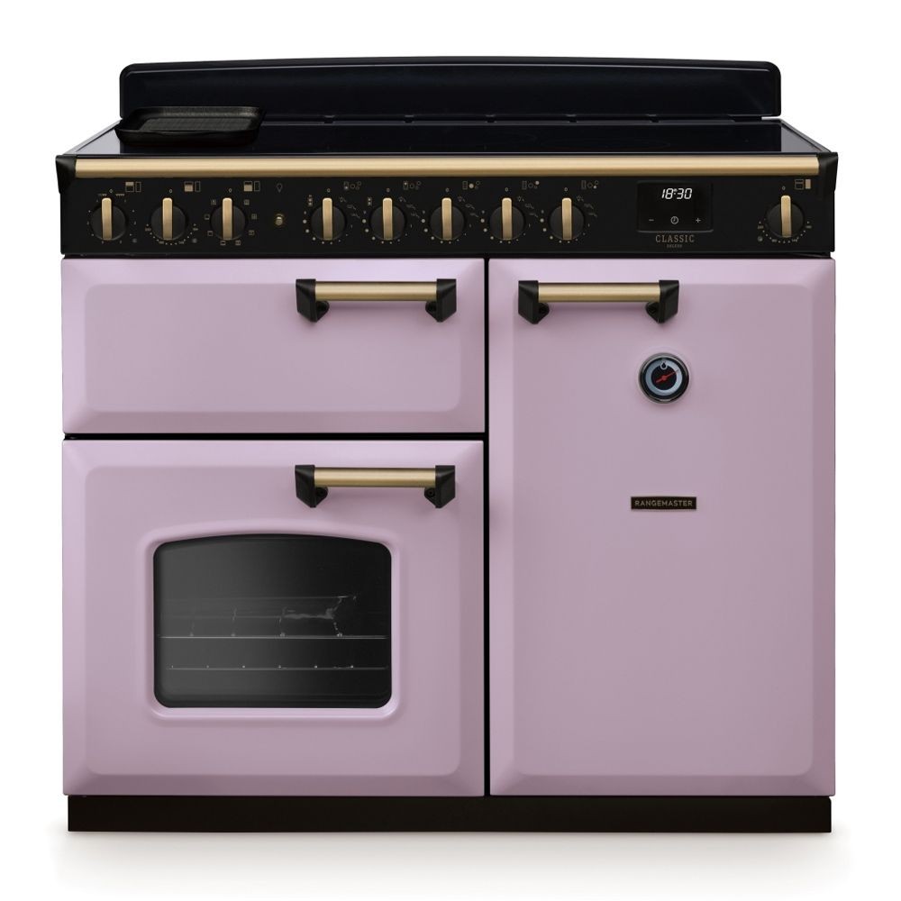 Classic Deluxe 100cm induction range cooker in heather pink with antique brass accents, featuring two ovens, a grill, and control knobs on the front.