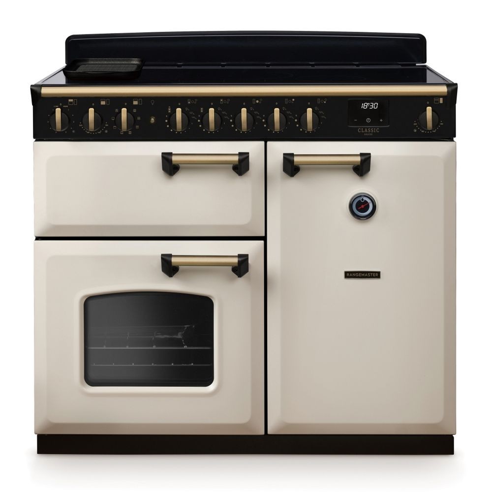 Classic Deluxe 100cm induction range cooker in pale cream with antique brass accents, featuring five control knobs, a digital display, and a large glass oven door.