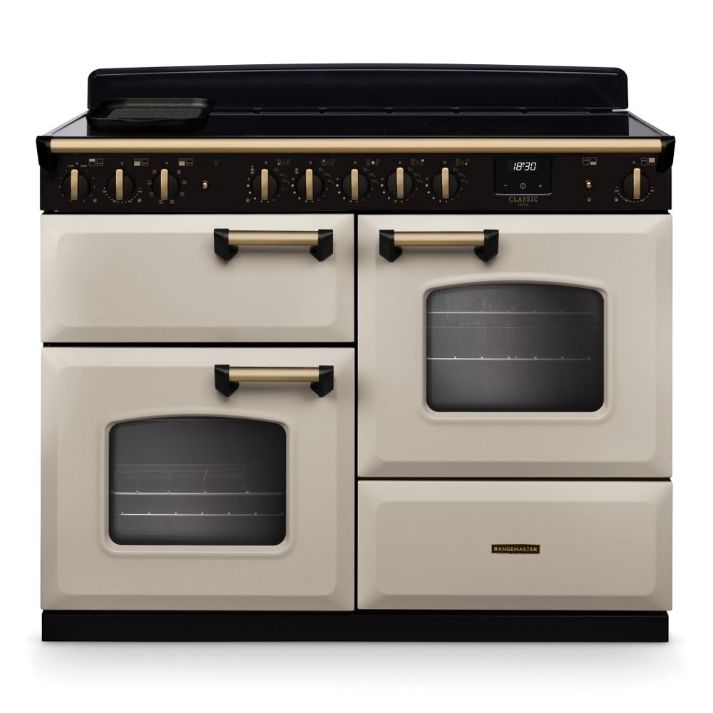 Classic Deluxe 110cm induction range cooker in pale cream with antique brass accents, featuring two ovens, six control knobs, and a digital display.