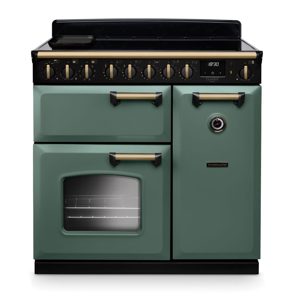 Classic Deluxe 90cm induction range cooker in mineral green with antique brass accents, featuring four control knobs, two ovens, and a sleek black top.