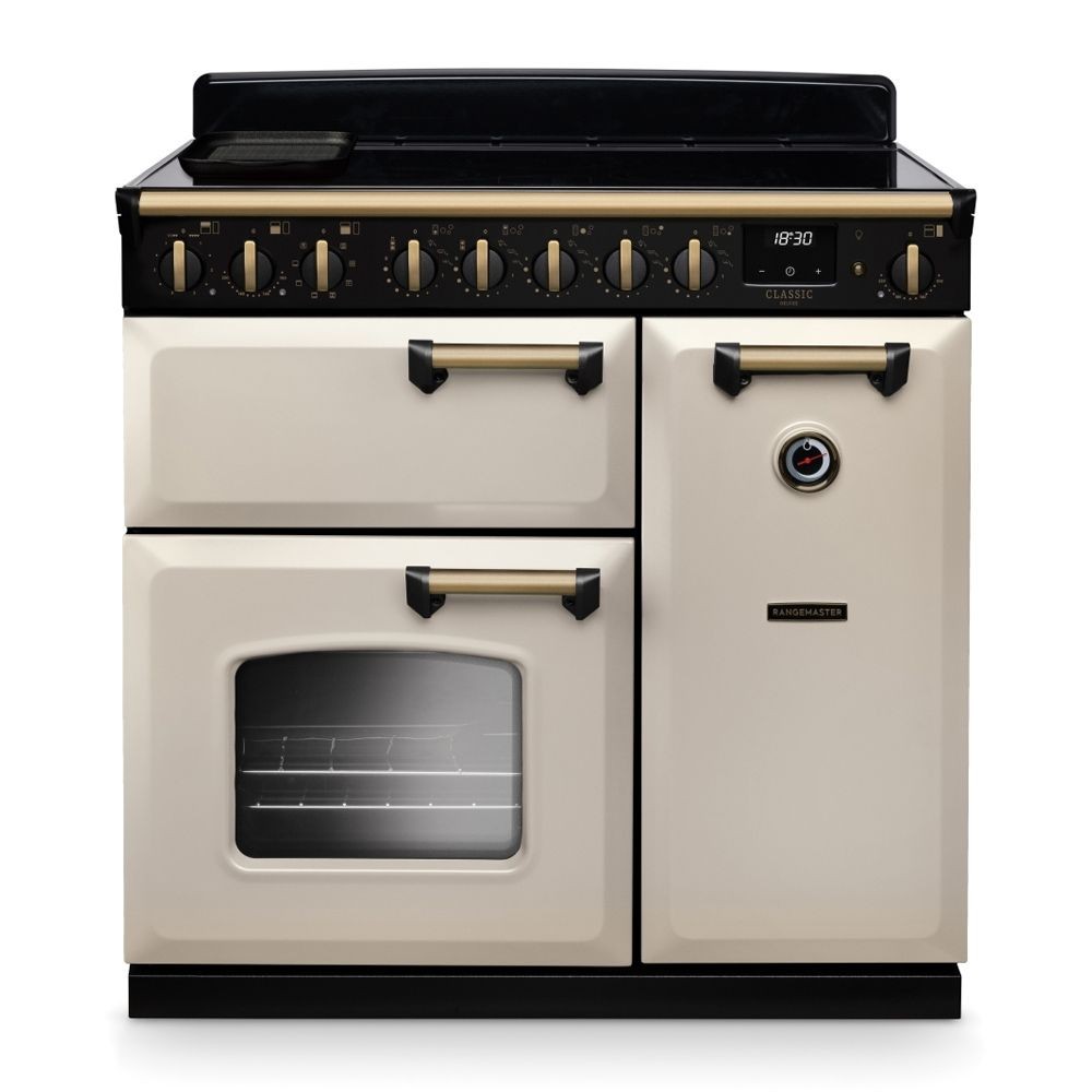 Classic Deluxe 90cm induction range cooker in pale cream with antique brass accents, featuring a black top, control knobs, and dual ovens with a glass door.