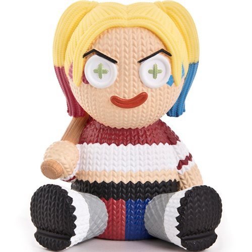 Collectible vinyl figure of Harley Quinn with blonde pigtails, red and blue accents, a striped shirt, and a bat, featuring large white eyes with green crosses, made of textured material.