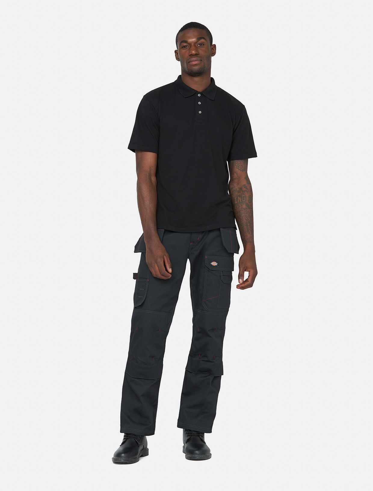 Black Dickies Men's Redhawk Pro Trousers featuring multiple pockets, reinforced knees, and a durable fabric, paired with a black polo shirt and black shoes.