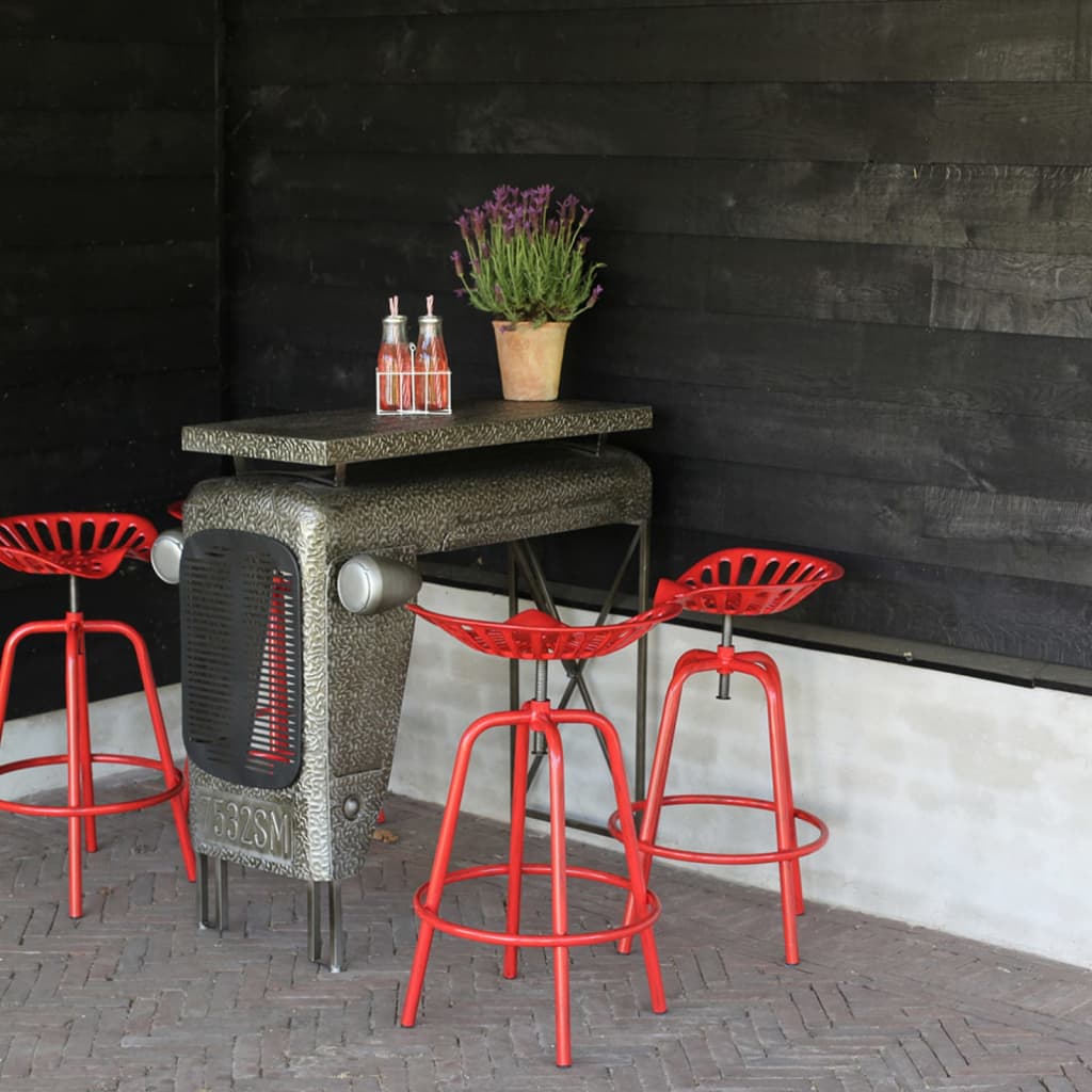 Red tractor-style chair with a metal frame and a unique seat design, paired with a matching table, set against a black wooden backdrop.