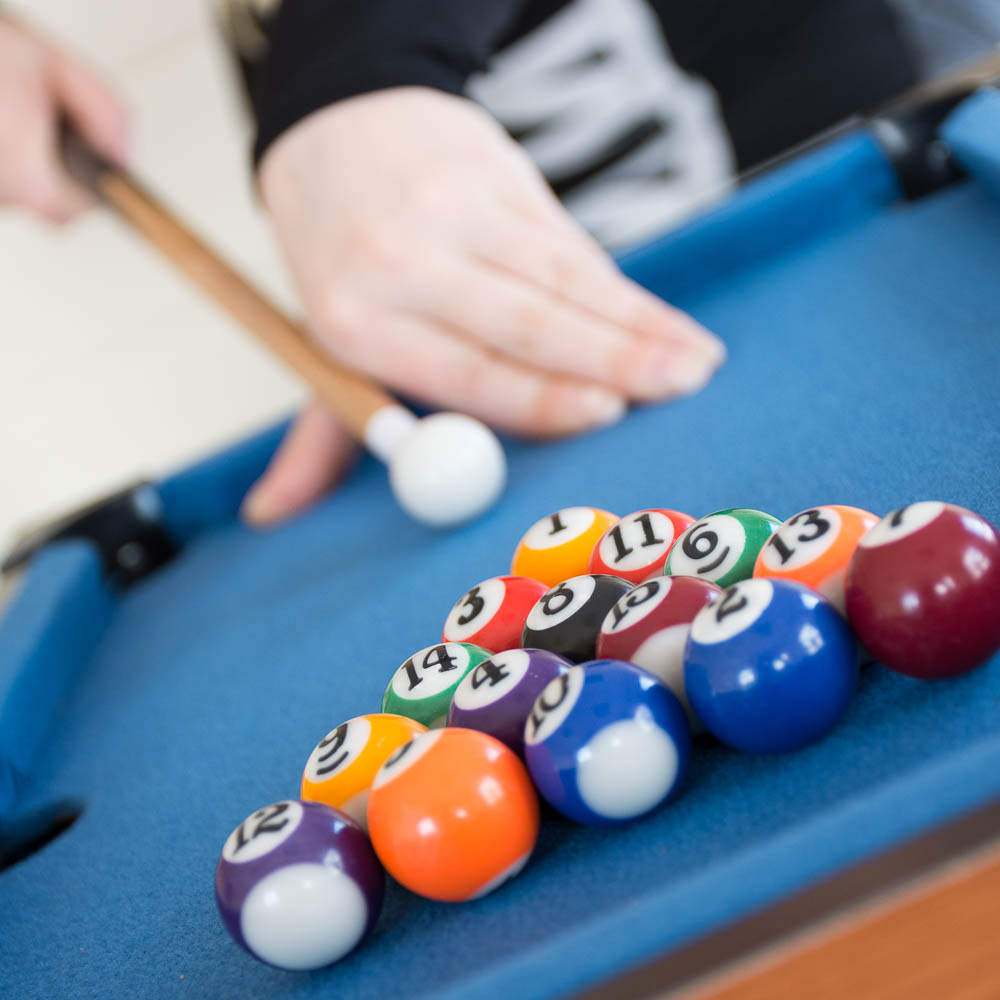 Mini pool table with a blue felt surface, featuring colorful billiard balls arranged in a triangle, and a cue stick poised for a shot.