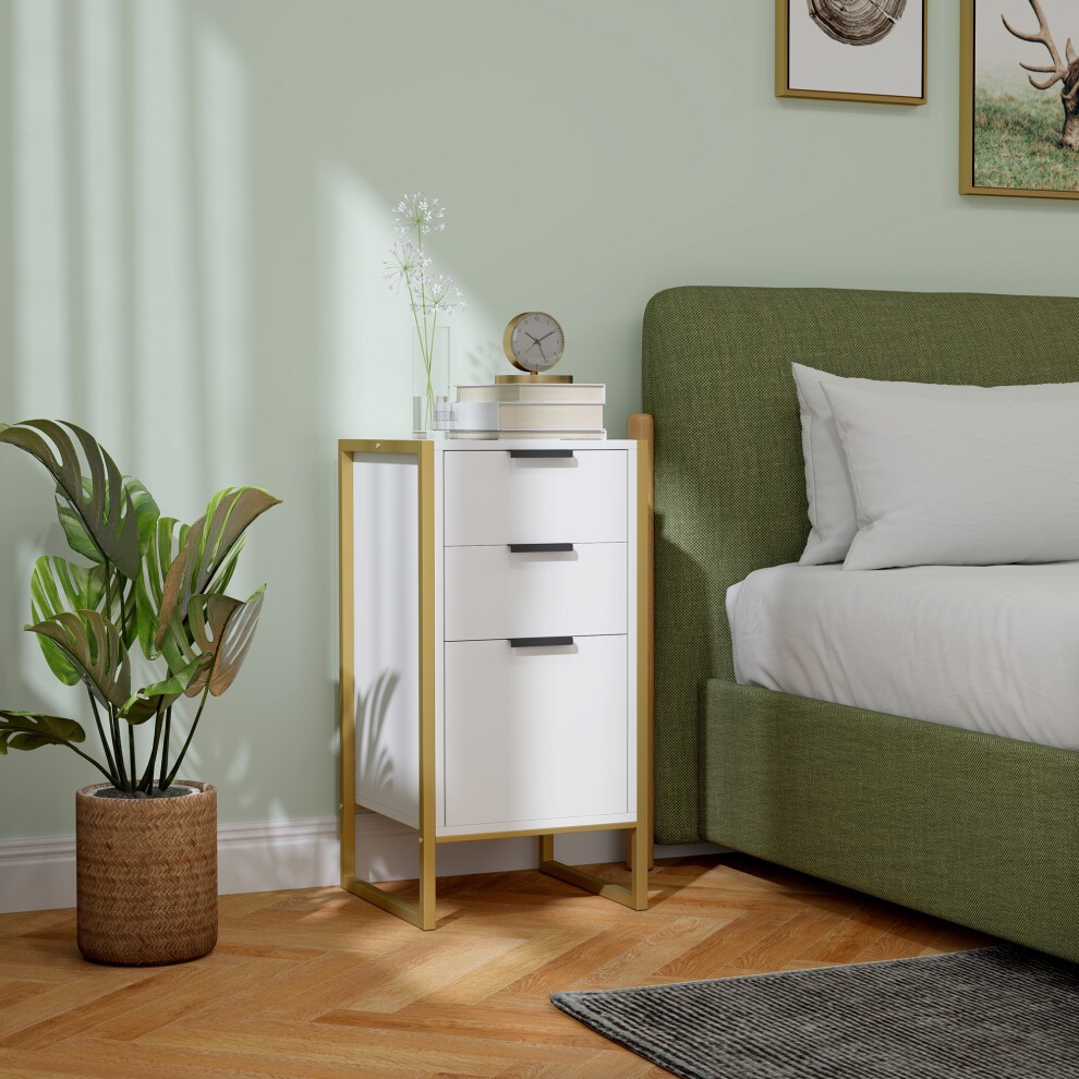 Industrial-style 3-drawer chest in white with a metal frame, featuring sleek handles, placed beside a green upholstered bed and a decorative plant in a woven basket.