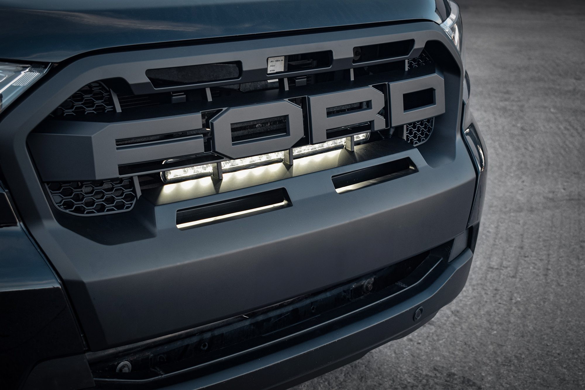 Black front grille of a Ford Ranger featuring a luminous LED integration kit with two bright white LED lights, designed for 2018-2022 models, highlighting the "FORD" logo.