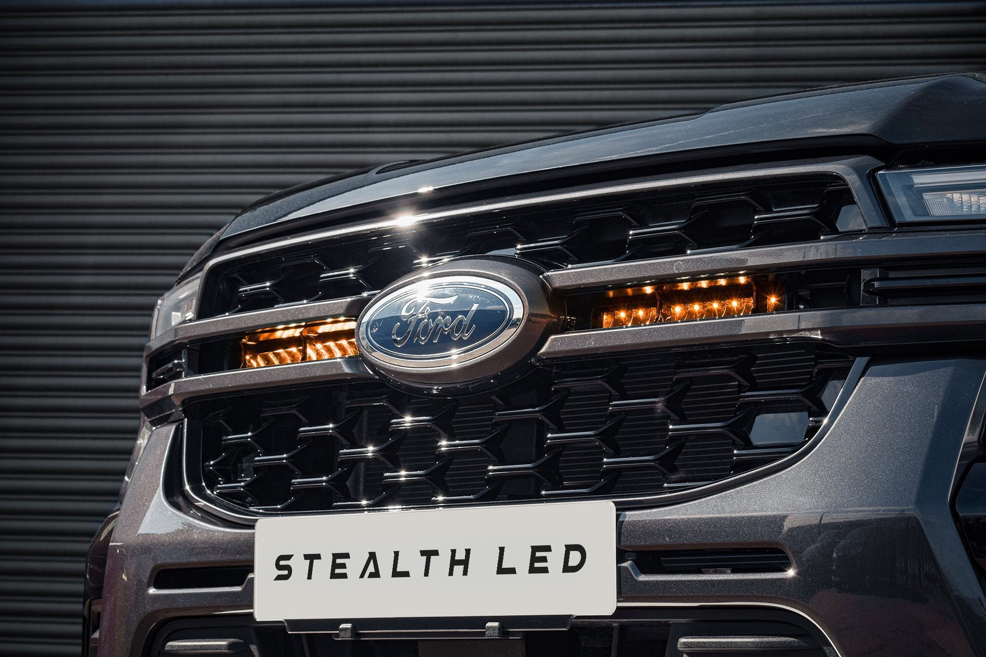 Black honeycomb grille featuring twin orange LED lights, showcasing the Stealth LED branding and Ford logo, designed for the 2023+ Ford Ranger T9 model.