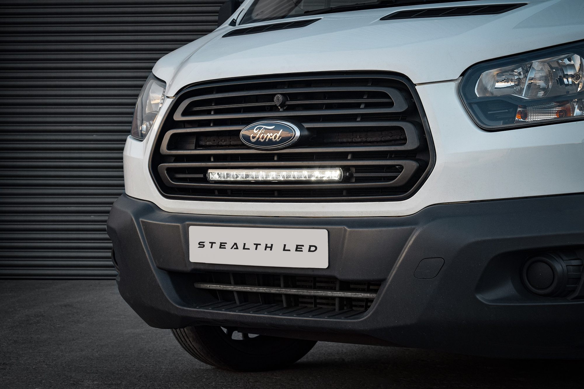 Luminous black grille kit for Ford Transit 2015-2019, featuring integrated white LED lights, with a sleek design and a prominent Ford emblem.
