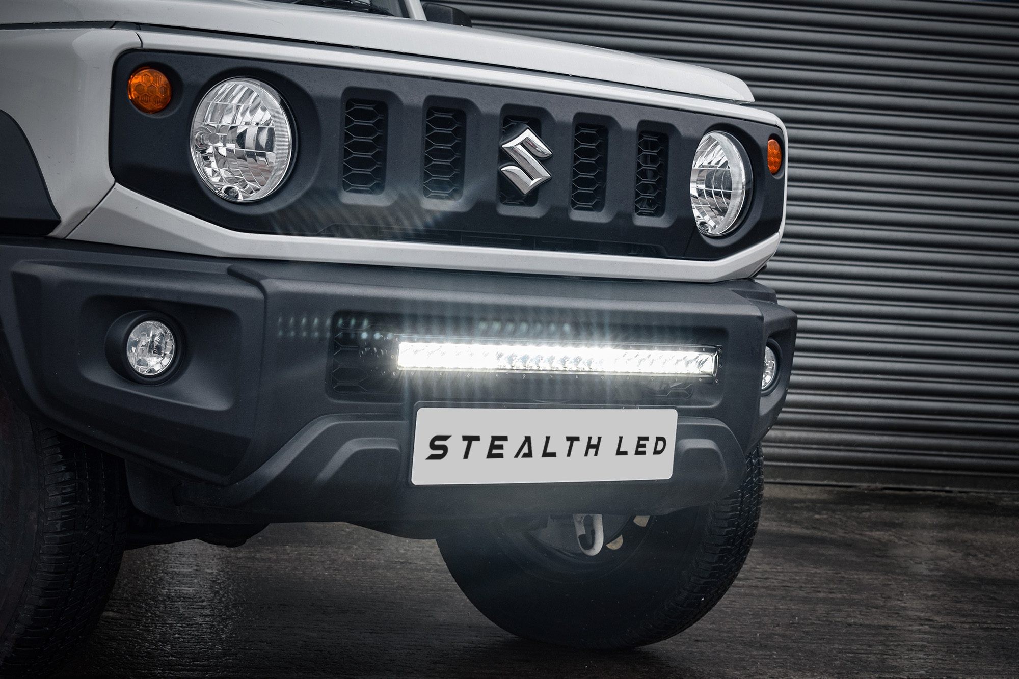 Luminous black grille kit for Suzuki Jimny 2018+, featuring integrated LED lights, 24,000 lumens, and a sleek design with a prominent logo and bright front lighting.