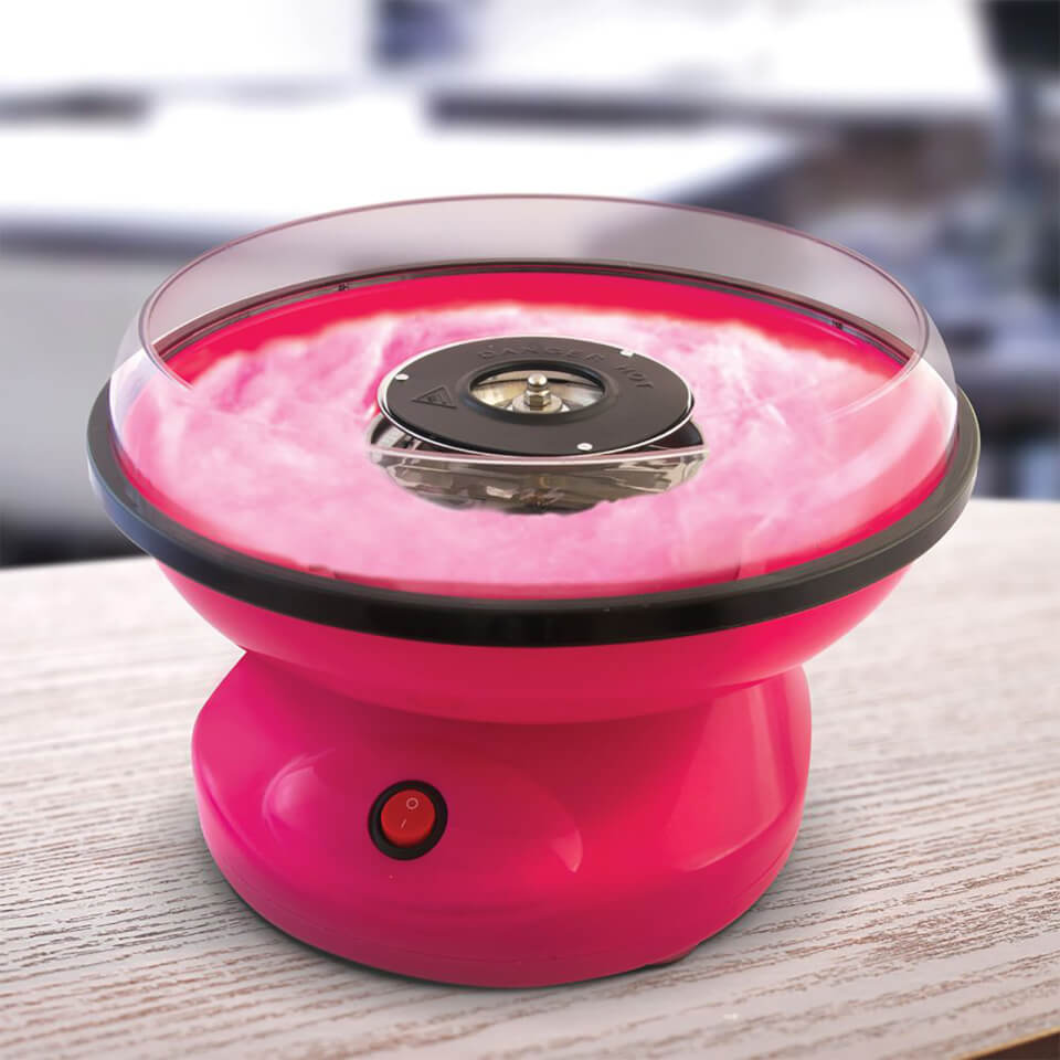 Bright pink candy floss maker with a transparent bowl, black rim, and a central spinning head, featuring an on/off switch on the base, set against a blurred background.