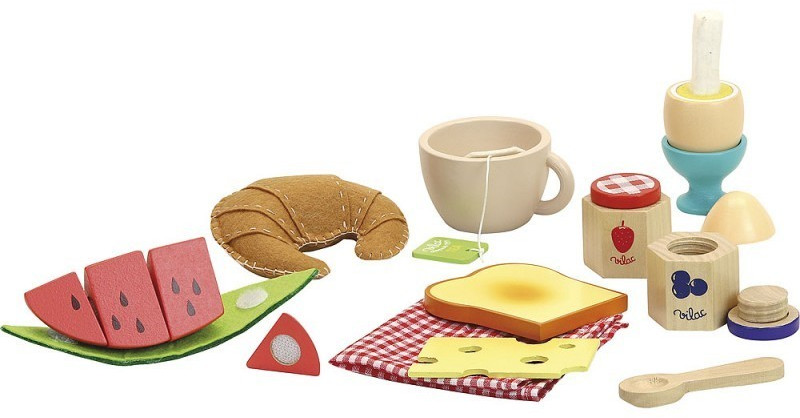 A colorful wooden breakfast food set featuring a croissant, toast, cheese, watermelon slices, an egg cup, a mug, and various accessories on a checkered cloth.