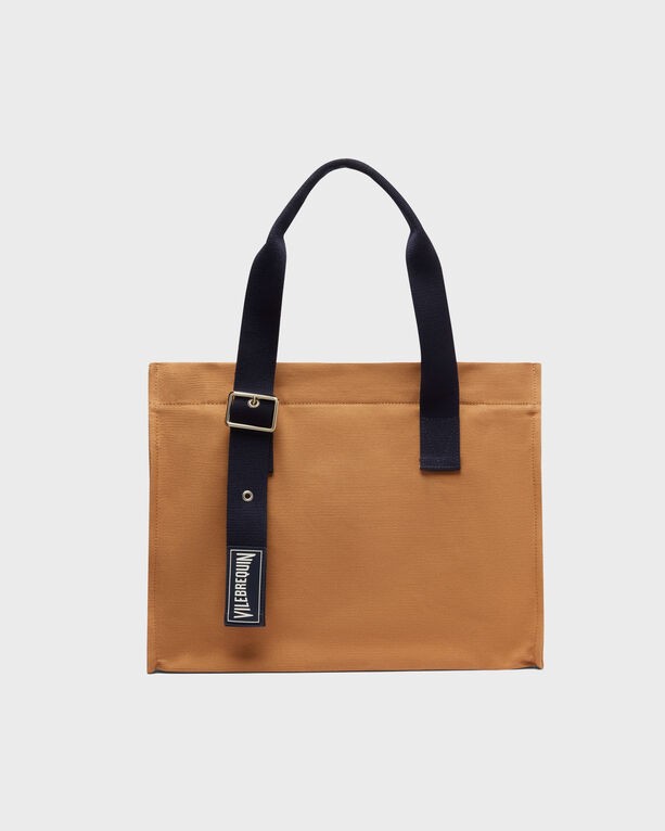 Brown cotton beach bag with navy blue handles and a logo tag, featuring a simple, solid design and an open top, suitable for various beach essentials.