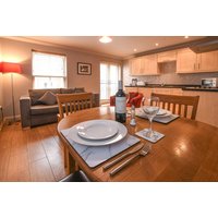 Dining table set for two in cozy apartment with sofa, wooden floors, modern kitchen, and warm lighting.