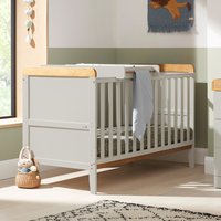 Dove grey cot bed with wooden accents, integrated changer, and mattress in a sunlit nursery.
