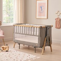 Gray and wood Tutti Bambini CoZee XL Bedside Crib with mesh sides and adjustable legs in a cozy nursery setting.