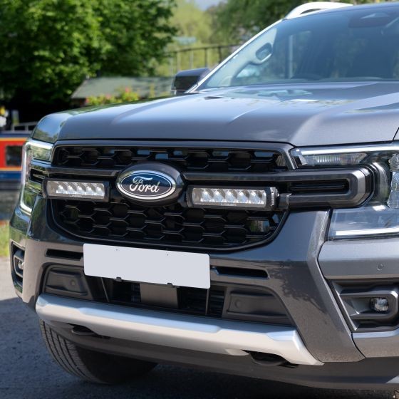 Lazer Lamps Grille Integration Kit features Gen 2 Triple-R 850 lamps mounted in a sleek black grille of a gray Ford vehicle, enhancing visibility and style.
