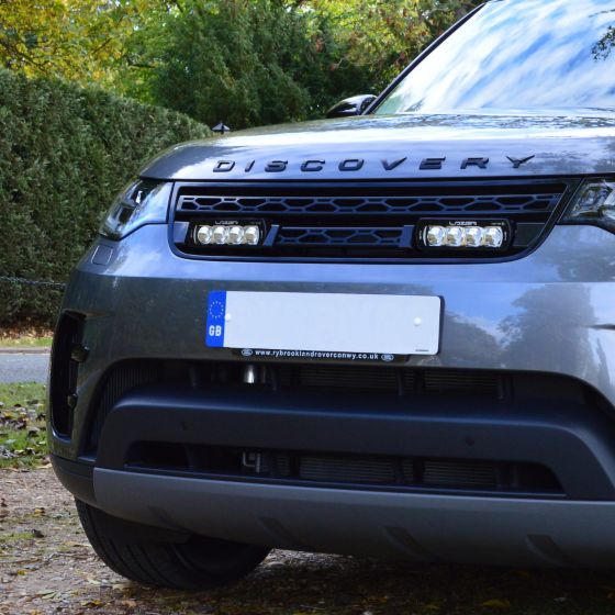 Lazer Lamps Grille Integration Kit featuring two sleek ST-4 Evolution Lamps, mounted on a grey vehicle's front grille, enhancing visibility with a modern design.