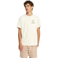 Beige cotton T-shirt with "Surf Club" text on chest, worn by model with curly hair, paired with plaid shorts.