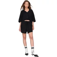 Black fluid shorts with elastic waist, paired with a matching button-up top, worn by a woman with socks and heels.
