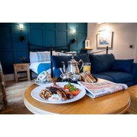 Breakfast spread with tea set on table, cozy hotel room with blue accents, bed, sofa, and wall art in background.