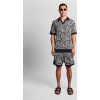 Blue ribbed knitted shorts with emblem design, worn by a model with matching patterned shirt and sandals.