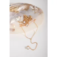 Gold multi-layer necklace with a crystal pendant, displayed on a shell background.