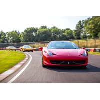 Red sports car leading on a racetrack with two yellow cars following, surrounded by greenery and clear skies.