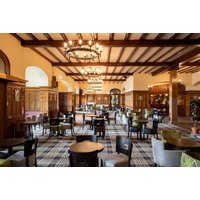 Hotel dining room with wooden beams, chandeliers, plaid carpet, and various seating arrangements.