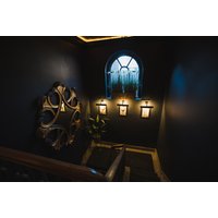 Dark hallway with ornate mirror, arched window, and warm wall lights at Impossible Motel.
