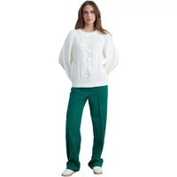 White thick knit jumper with cable pattern, long sleeves, worn by a woman with green pants.