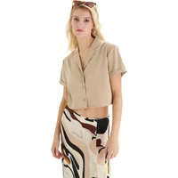 Beige short-sleeve button-up shirt with collar, worn by woman, paired with abstract patterned skirt.