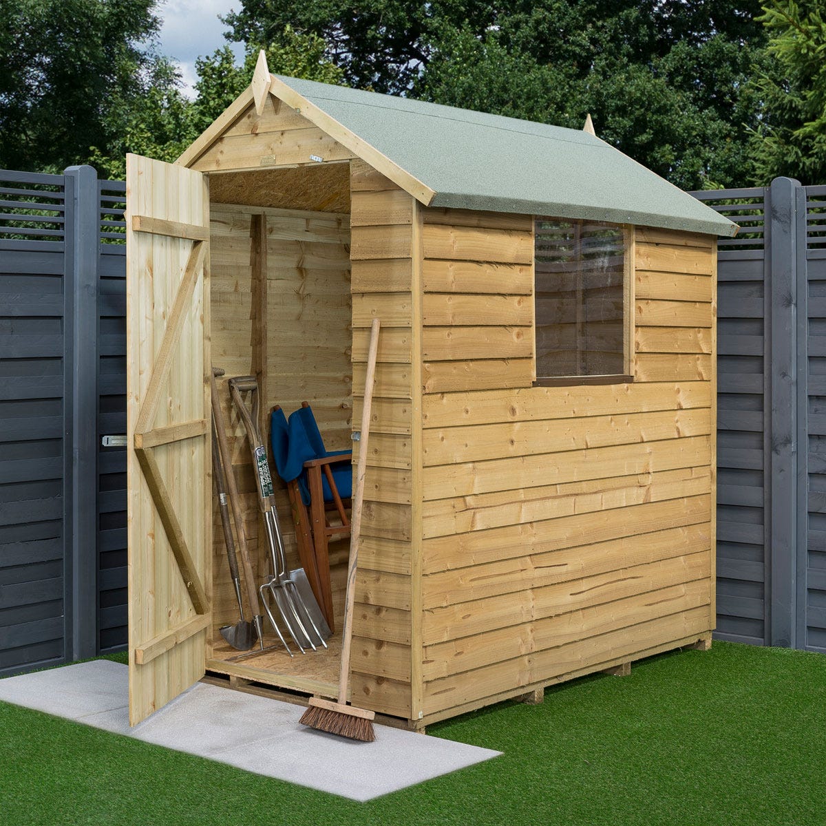 Wooden shed with a green felt roof, featuring overlapping timber panels, a front door, a window, and gardening tools visible inside on a concrete base.