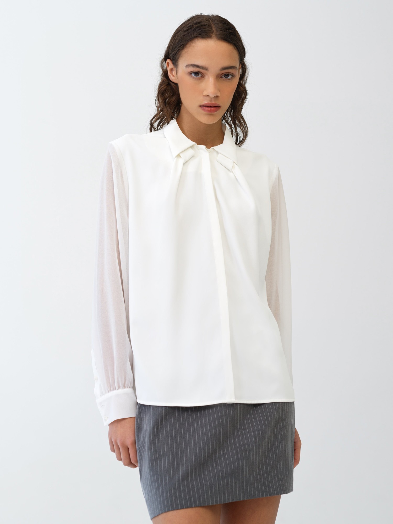 White crepe shirt featuring a collar detail, long sheer sleeves, and a front pleat, paired with a gray pinstriped skirt for a chic, sophisticated look.