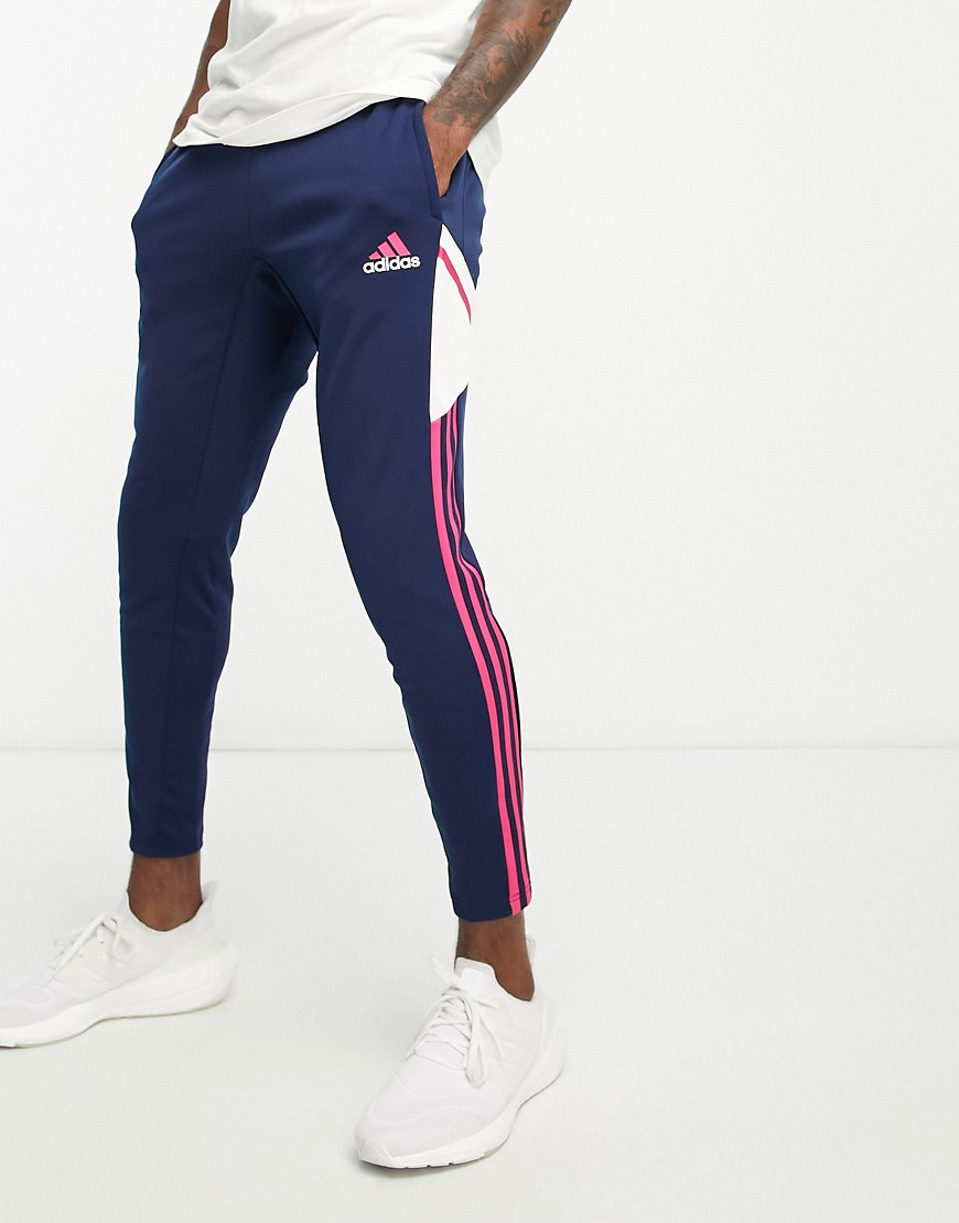 Navy training pants featuring pink Adidas stripes, a white side panel, and a tapered fit, made from lightweight, breathable material.