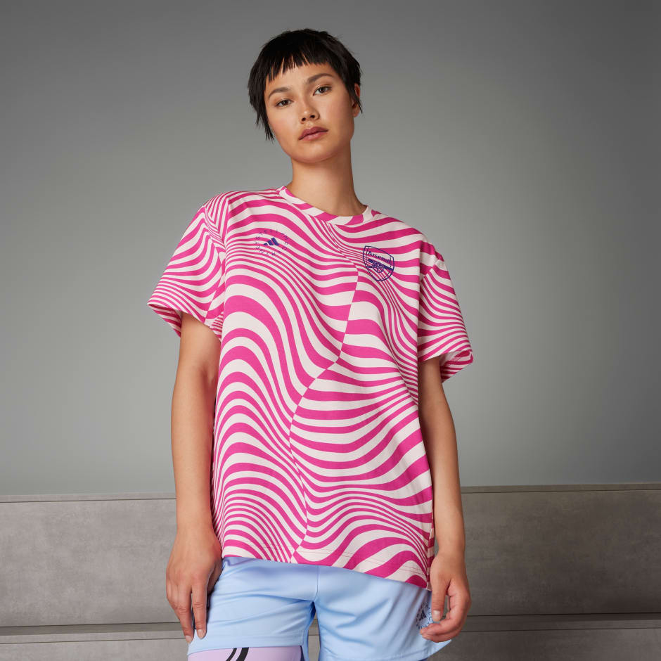 Pink and white striped women's tee featuring a round neckline, short sleeves, and an Arsenal logo, paired with light blue shorts for a sporty look.