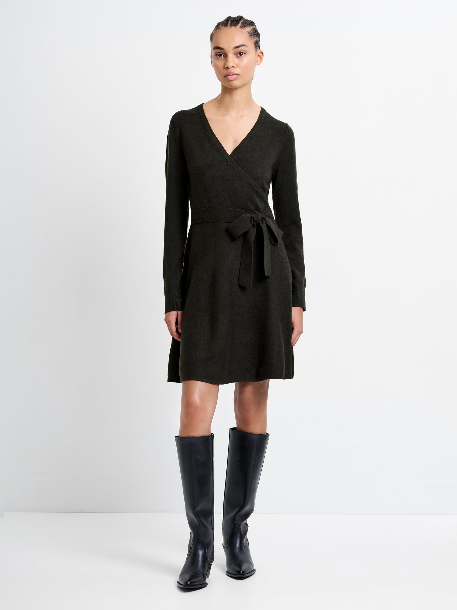 Dark green Babysoft Wrap Mini Dress by French Connection, featuring a V-neck, long sleeves, a tie waist, and a flared skirt, paired with knee-high black boots.