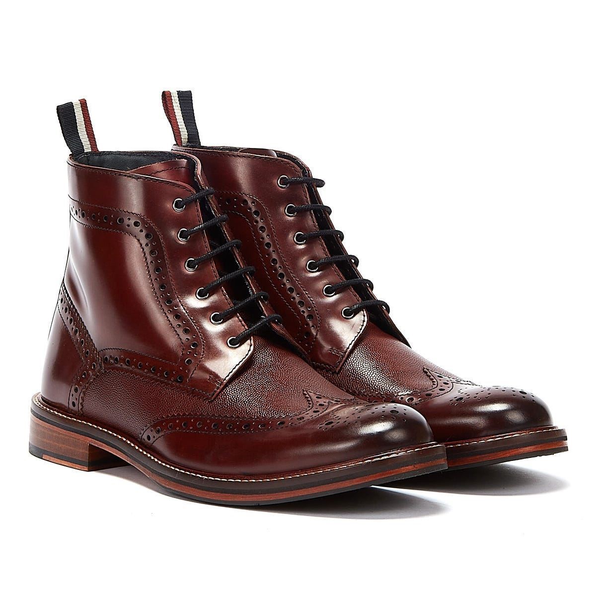 Burgundy leather brogue boots featuring intricate perforations, a lace-up front, and a stacked wooden heel, with contrasting pull tabs at the back.