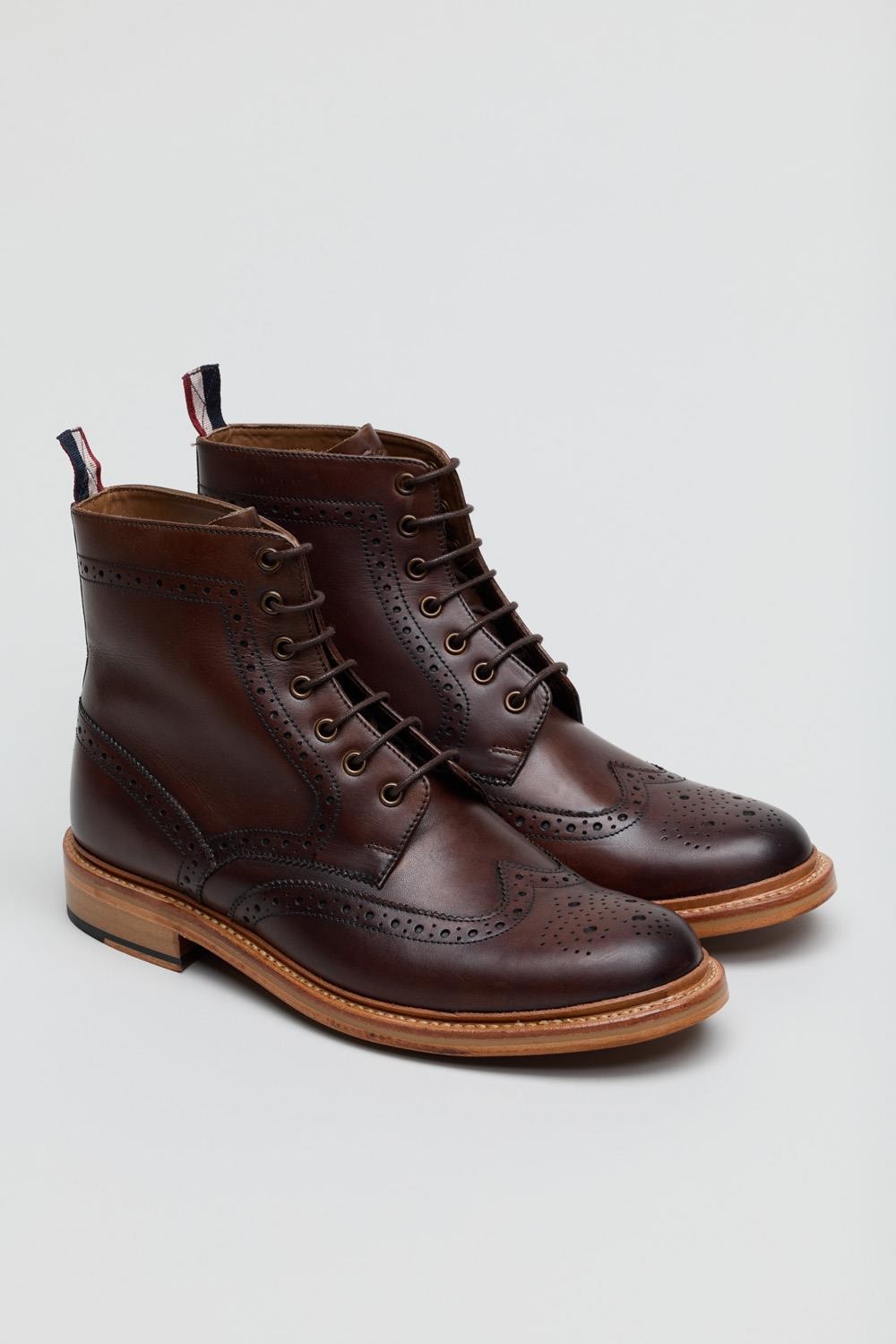 Brown leather men's boots featuring brogue detailing, lace-up front, and a contrasting tan sole with a red, white, and blue pull tab.