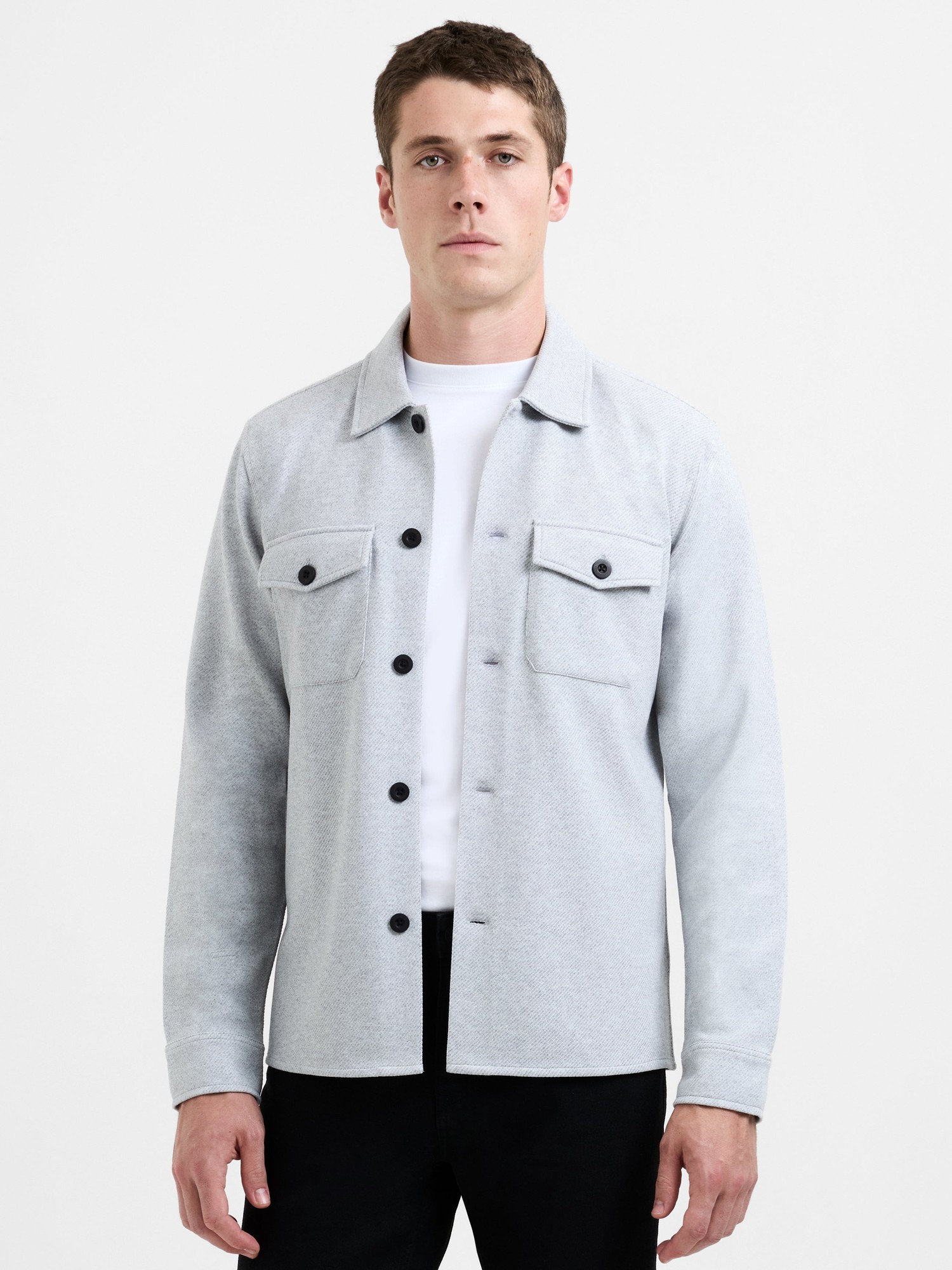Heather grey canvas jersey overshirt featuring a button-up front, two chest pockets, and a relaxed fit, paired with a white crew neck t-shirt and black pants.