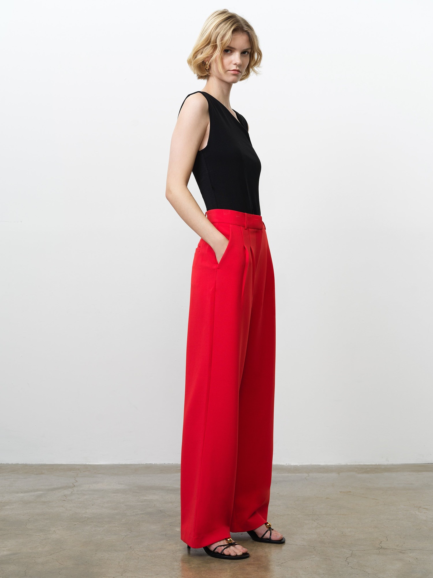 Tailored wide-leg trousers in vibrant red, featuring a high waist, pleated front, and side pockets, styled with a fitted black tank top and strappy sandals.