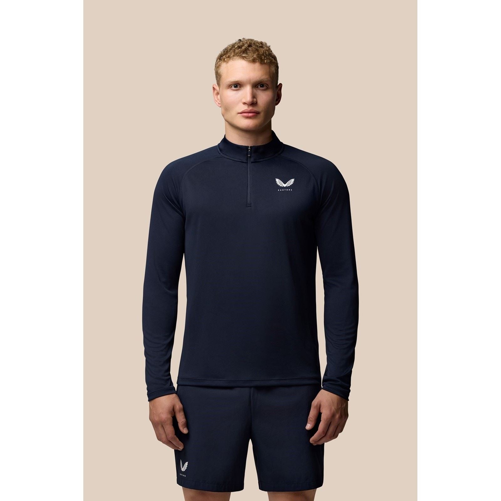 Men's blue polyester activewear 1/4 zip top featuring a high collar, long sleeves, and a small Castore logo on the chest, paired with matching shorts.