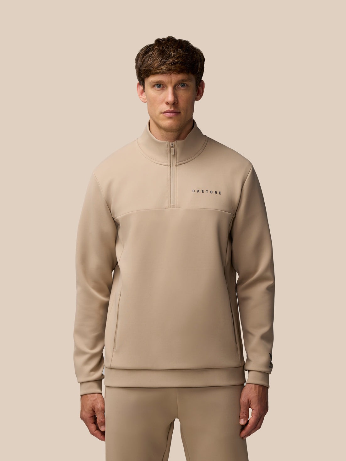 Brown polyester sweatshirt featuring a 1/4 zip, high collar, and embroidered "Castore" logo on the chest, designed for a sleek, modern look.