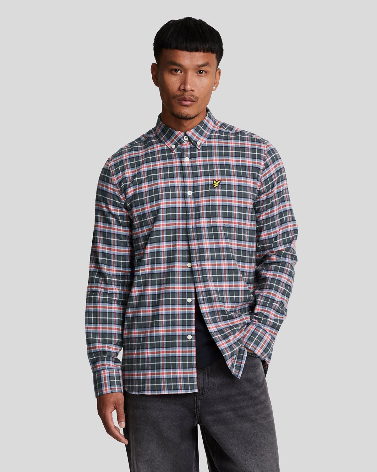 Checked flannel shirt in navy, green, and pink with a button-down collar and Lyle & Scott logo on the chest, paired with dark jeans.