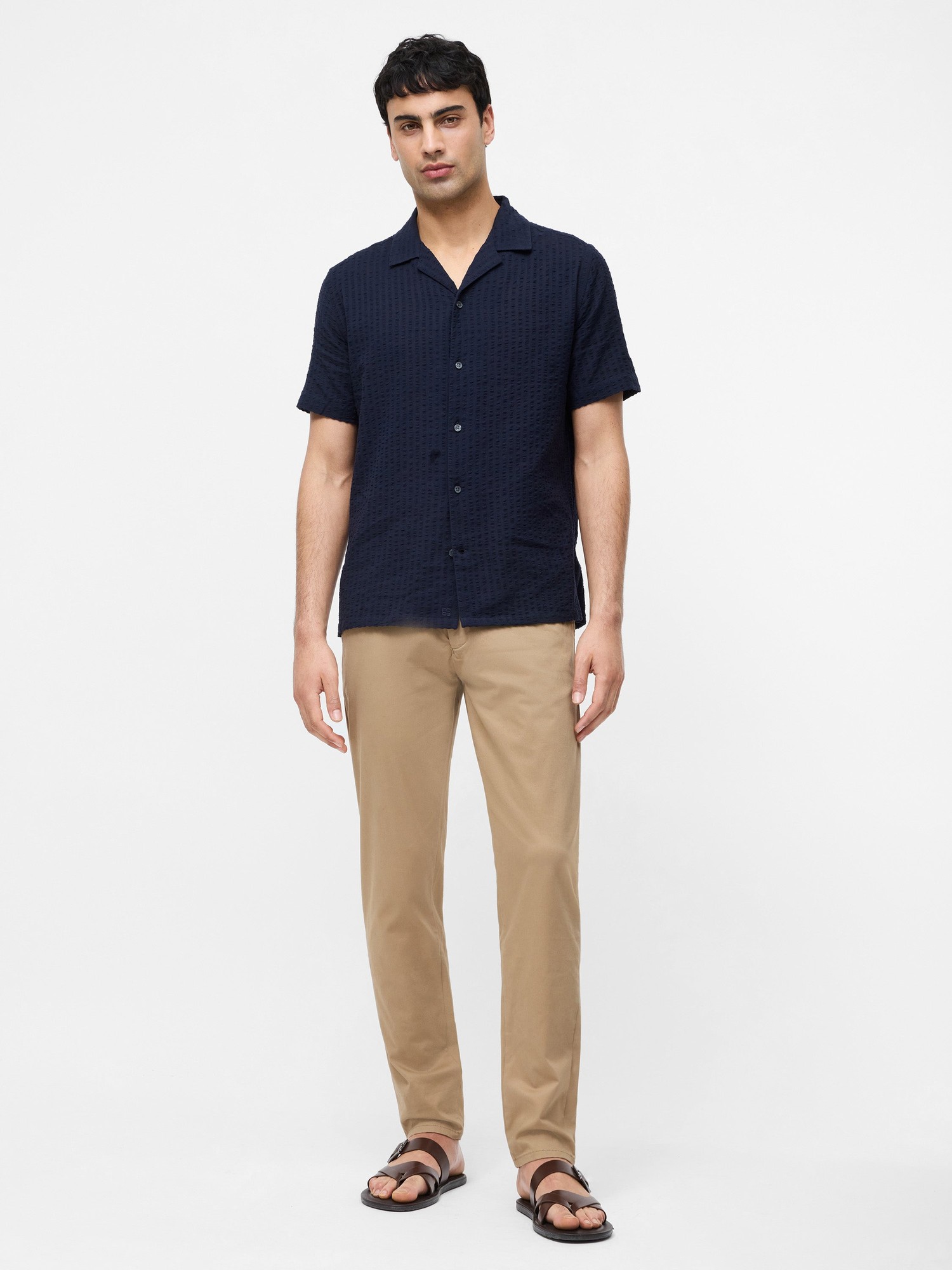 Light tobacco cotton stretch chinos in a regular fit, featuring a smooth texture and a 32-inch inseam, paired with a navy short-sleeve shirt and sandals.
