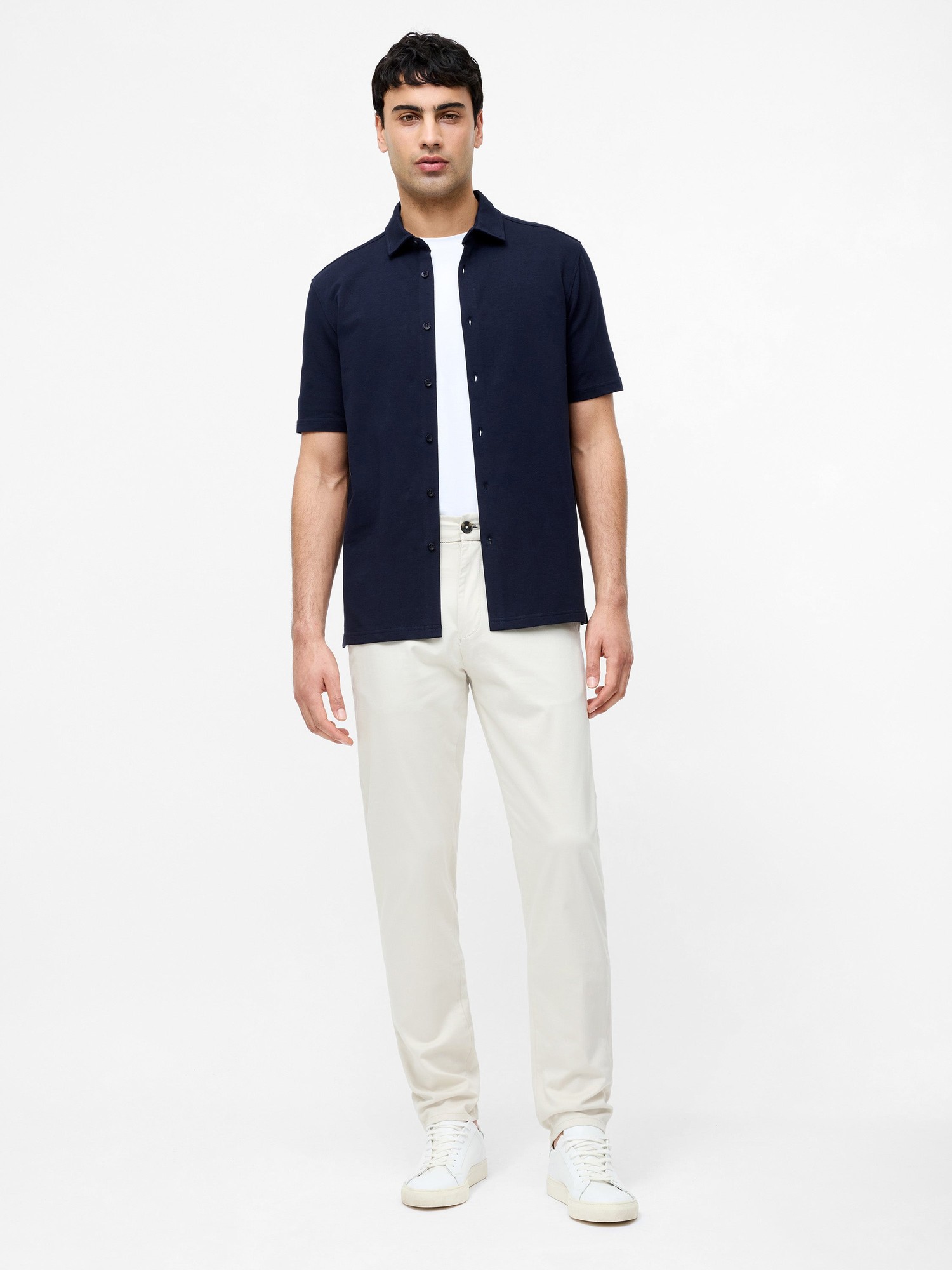 Light stone-colored cotton stretch chinos with a regular fit, paired with a navy short-sleeve shirt and white sneakers.