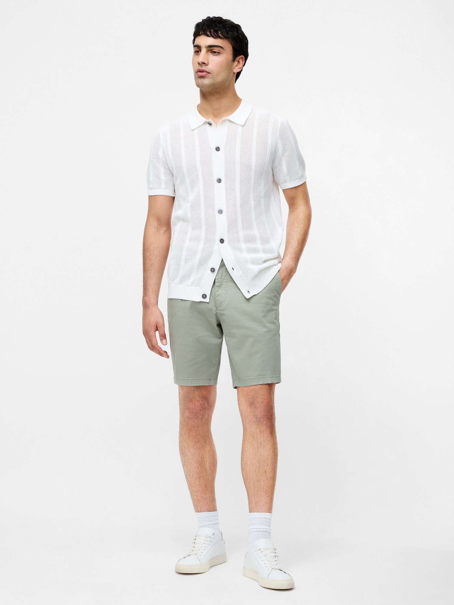 Sage green cotton stretch chino shorts, featuring a tailored fit, side pockets, and a smooth finish, paired with a white striped button-up shirt.
